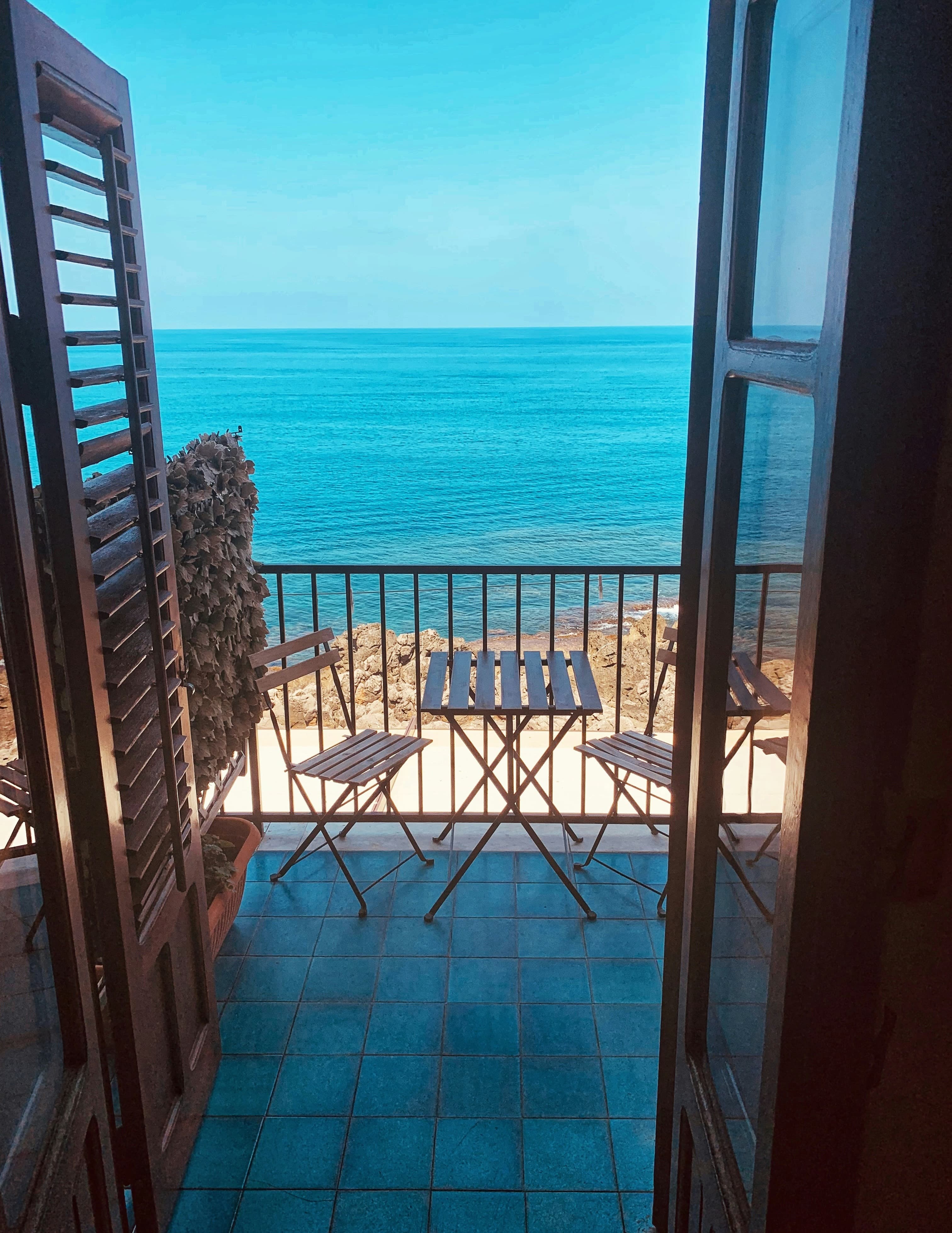 Open shutters looking out from a Mediterranean balcony onto the sea — a view from a home in the Kasero network